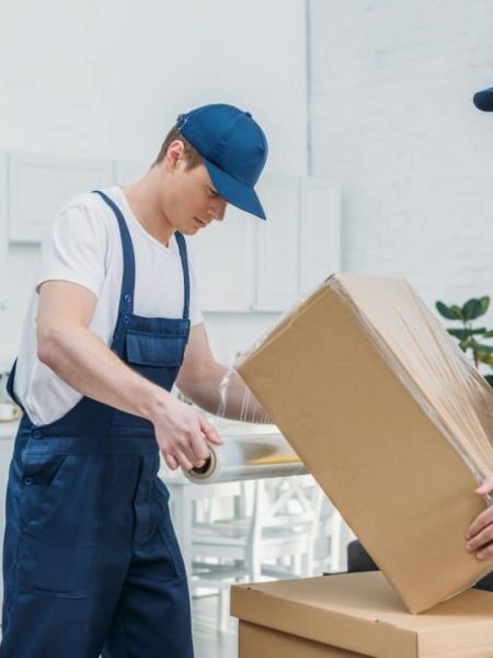 handsome-movers-wrapping-cardboard-box-with-stretch-film-in-apartment.jpg